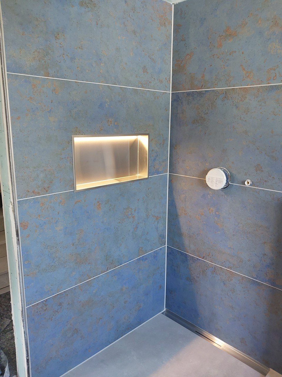 Dusche mit großformatigen Wandfliesen in blauer Rostoptik, beleuchteter Edelstahlnische und Bodenablaufrinne