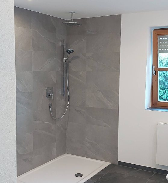 Dusche mit Regenbrause und großformatigen Wandfliesen in Steinoptik