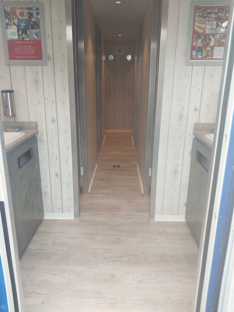 Mittelgang im Sanitärcontainer mit Waschplätzen links und rechts und Wandverkleidung in heller Holzoptik