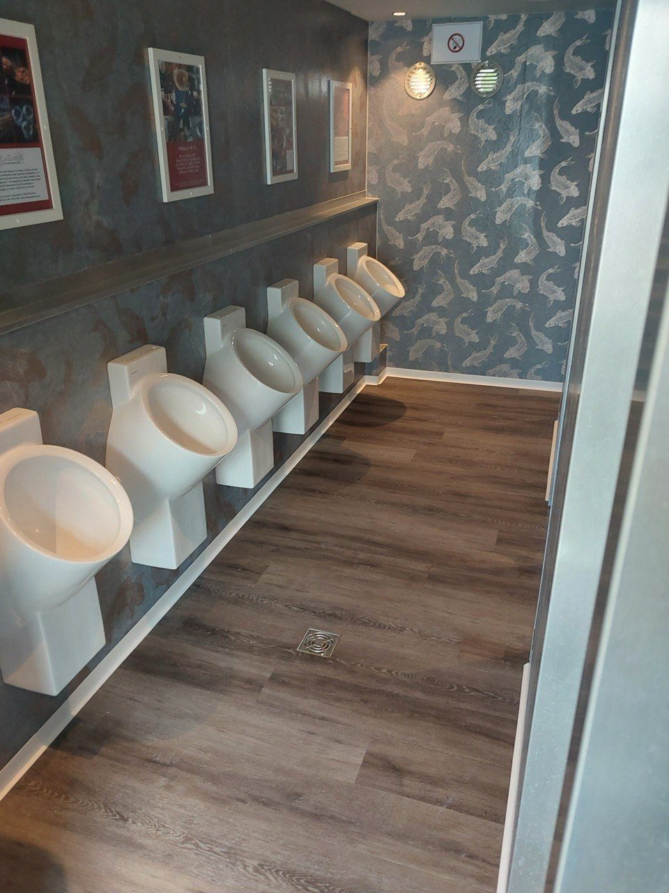 Herrenbereich mit sechs Urinalen, Koi-Tapete und gerahmten Bildern